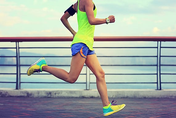 Woman running by the water in neon athletic clothes, watch, and armband