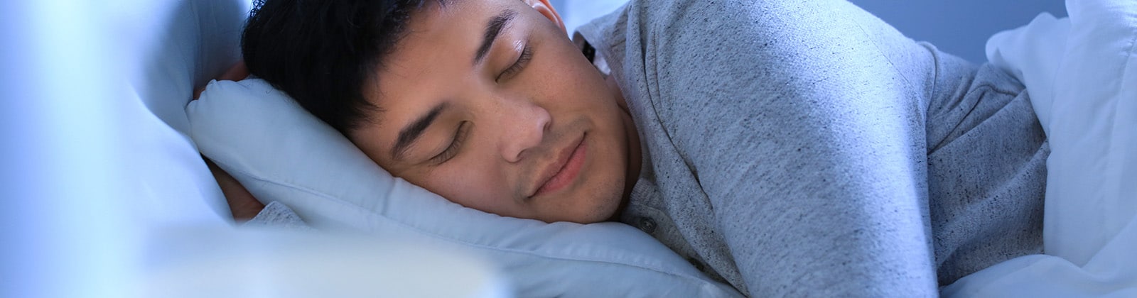 Asian man sleeping on side with eyes closed and slight smile