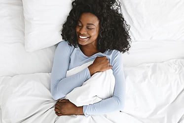 A black woman hugging the sheets in her bed