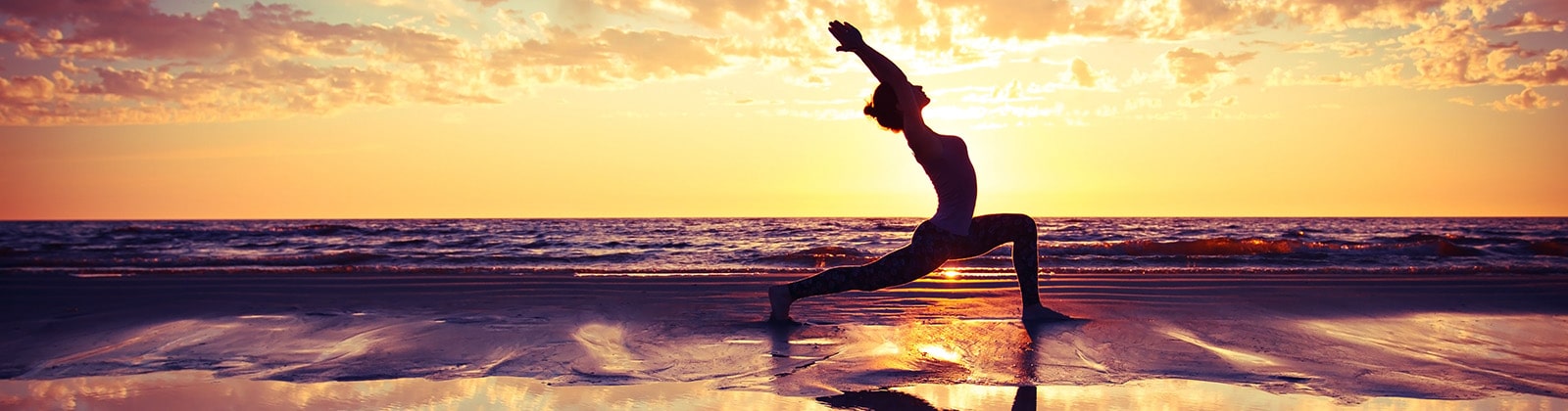 Woman doing yoga on the beach at sunset
